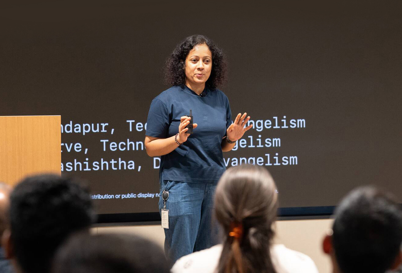 A speaker presenting to a seated audience in front of a large screen at an Apple Developer Center.